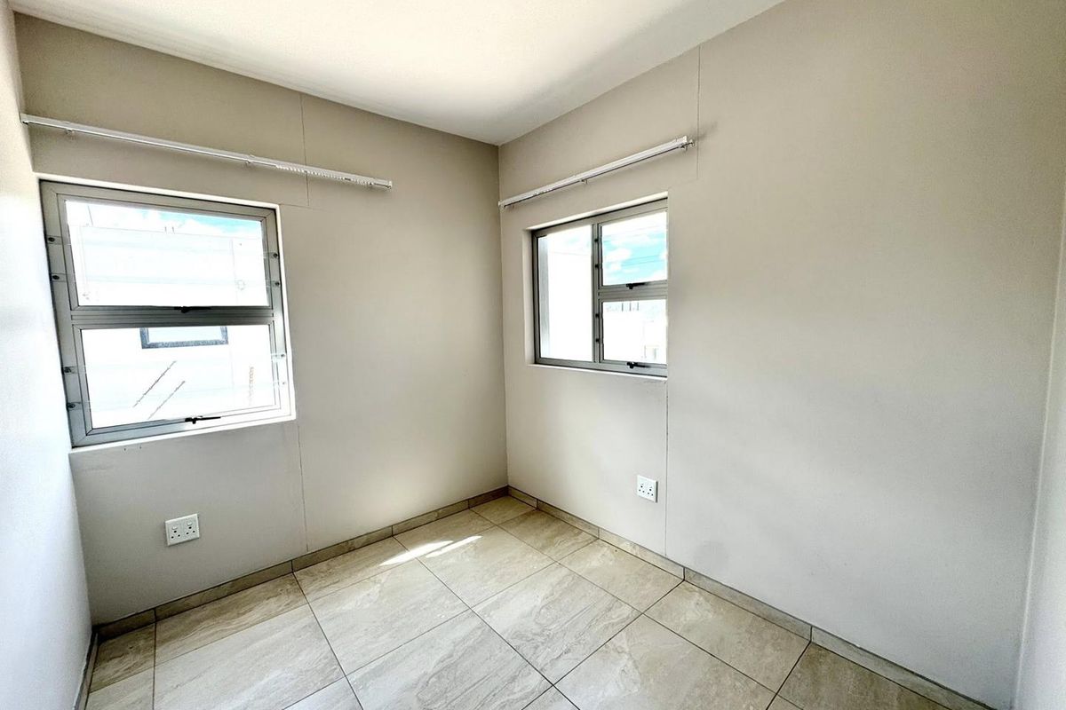 A bright, empty bedroom featuring neutral wall finishes, tiled flooring, and aluminium-framed windows, providing a clean and versatile space.