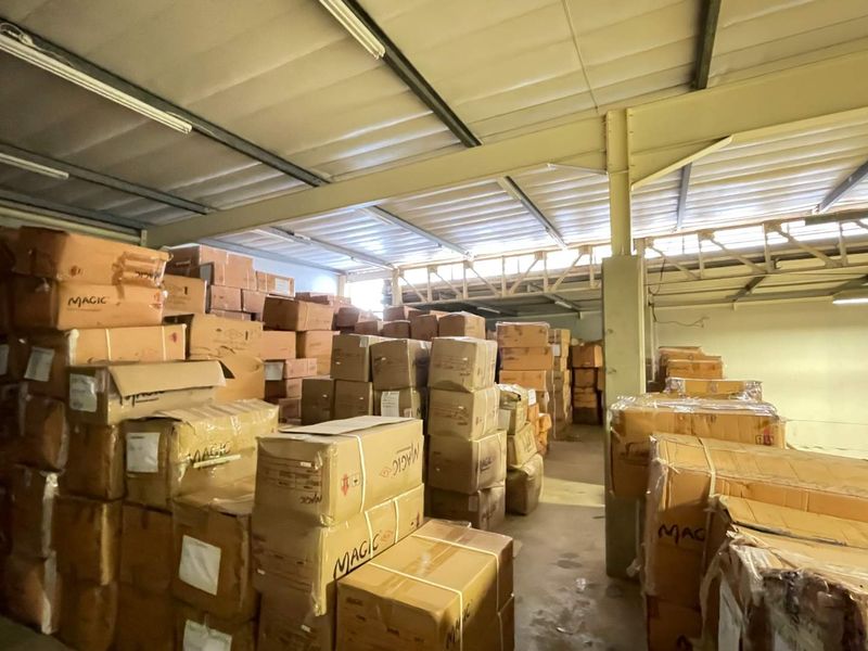A large industrial utility or storage space featuring exposed steel roof trusses, concrete flooring, and functional overhead lighting.