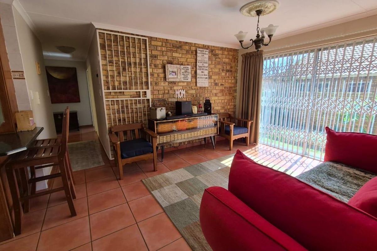 A living room featuring terracotta floor tiles, a brick feature wall, and sliding glass doors with security gates leading to the exterior.
