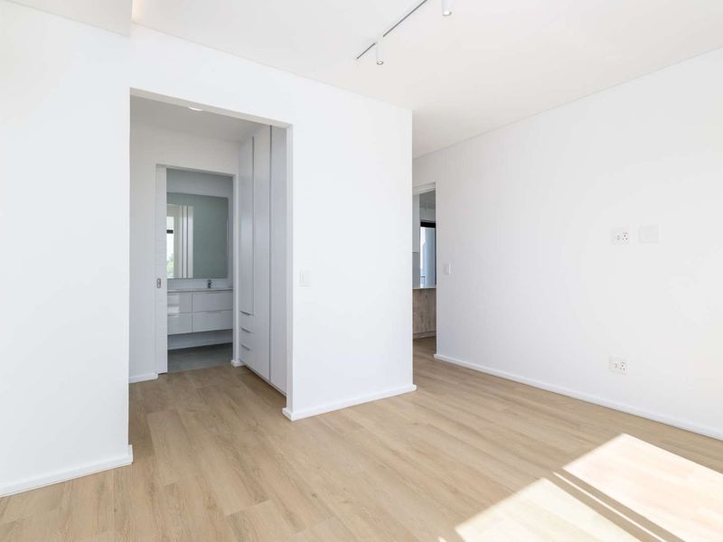 A bright, modern, and empty bedroom featuring light laminate flooring, built-in cupboards, and direct access to an en-suite bathroom.