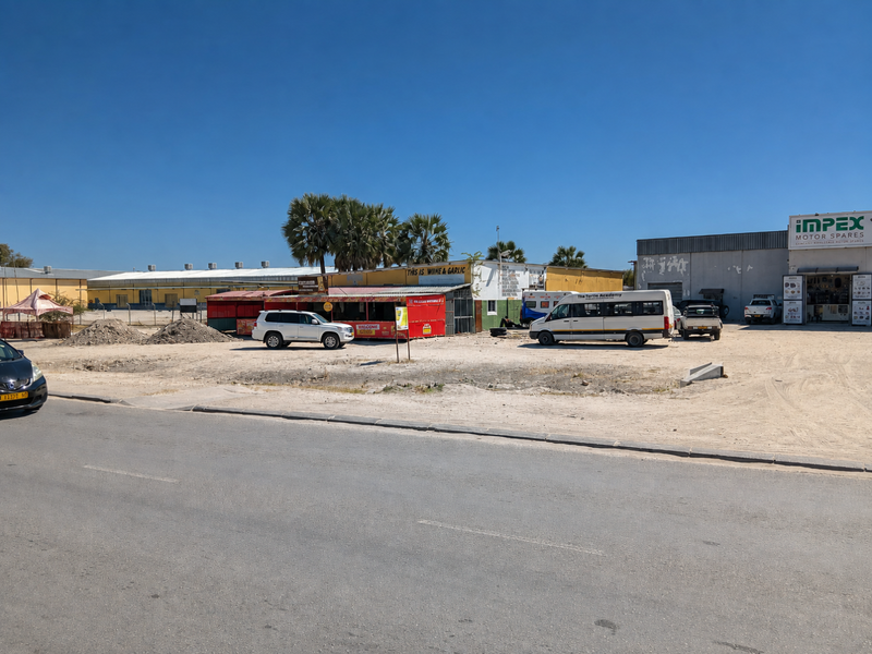 Front view of a commercial property featuring warehouse structures, a large unpaved parking area, and surrounding perimeter fencing.
