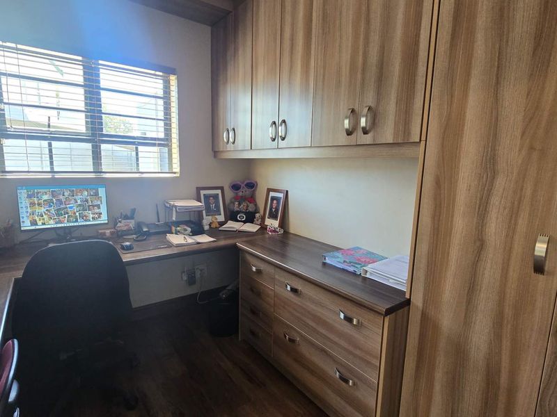 A functional home office featuring extensive built-in cabinetry, a spacious desk area, and integrated storage solutions with wood-grain finishes.