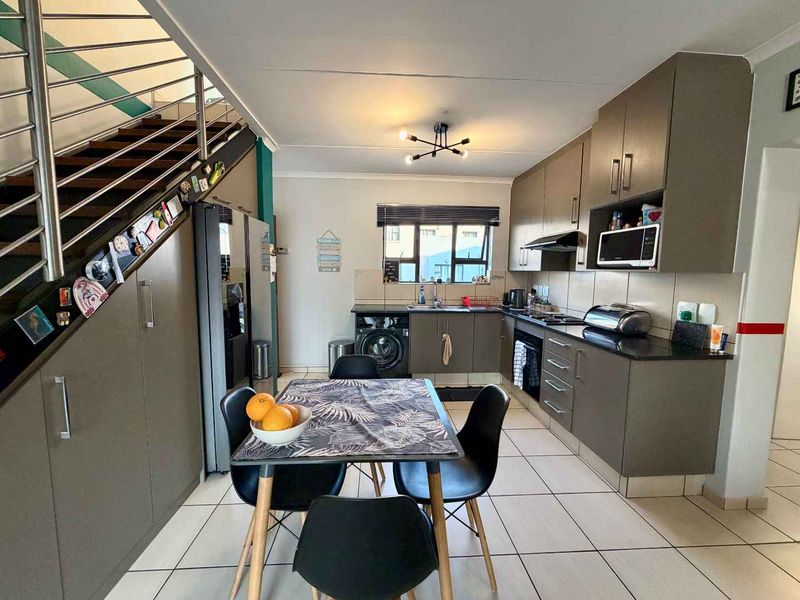 Open-plan kitchen and dining area featuring modern cabinetry, granite countertops, integrated appliances, and a staircase with a stainless steel balustrade.