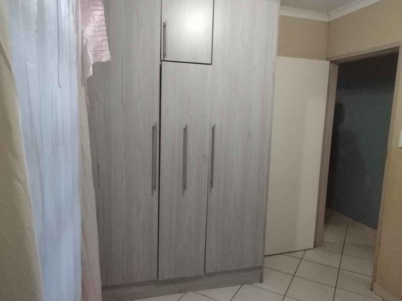 A bedroom featuring light wood-grain built-in cupboards and neutral tiled flooring, providing a clean and functional storage space.