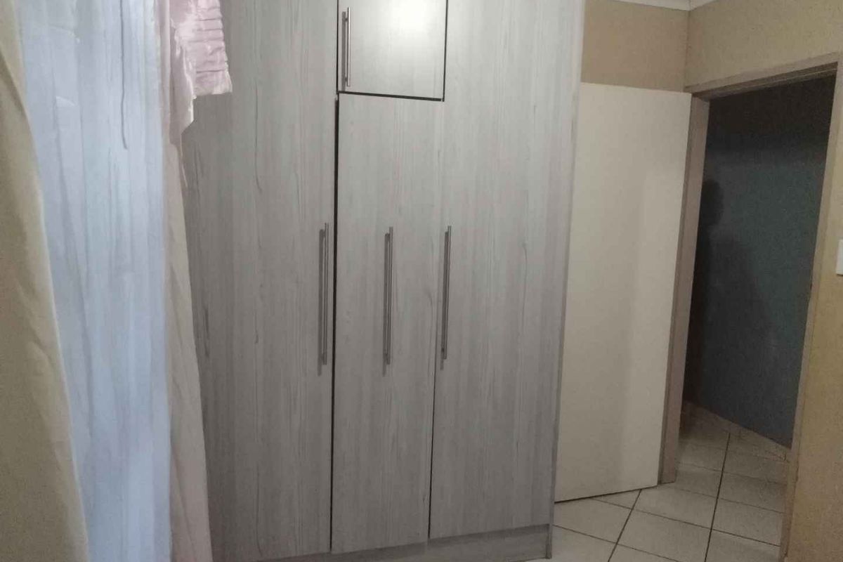 A bedroom featuring light wood-grain built-in cupboards and neutral tiled flooring, providing a clean and functional storage space.