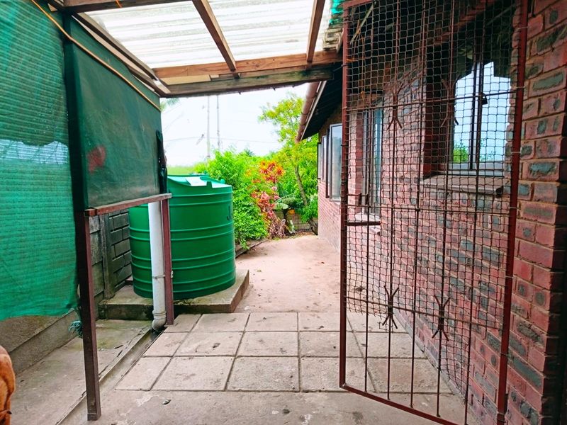 Rear exterior area featuring a paved patio, water storage tank, and covered walkway with security gate access.