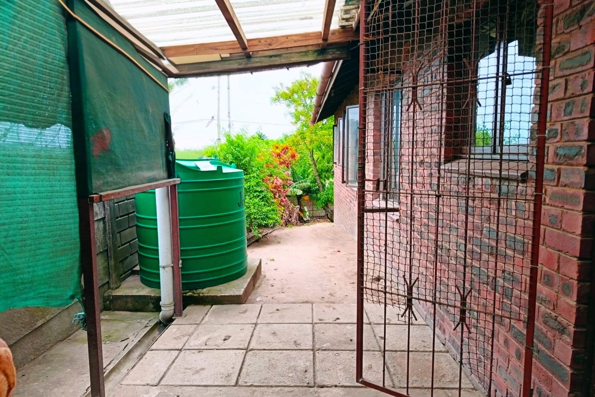 Rear exterior area featuring a paved patio, water storage tank, and covered walkway with security gate access.