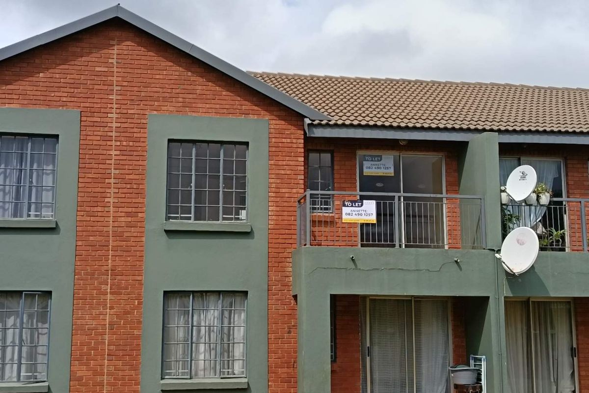 Rear view of a two-story brick apartment building featuring a balcony with metal railings and sliding glass doors.