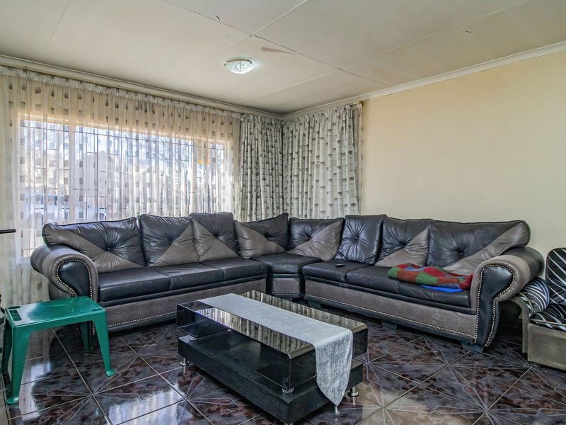 A living room featuring dark tiled flooring and window security bars, showing visible signs of ceiling wear and water staining.