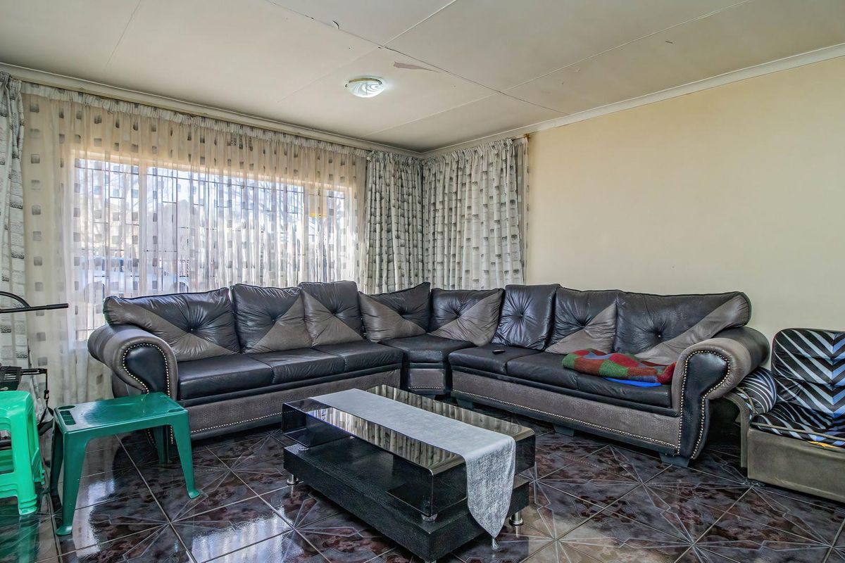 A living room featuring dark tiled flooring and window security bars, showing visible signs of ceiling wear and water staining.