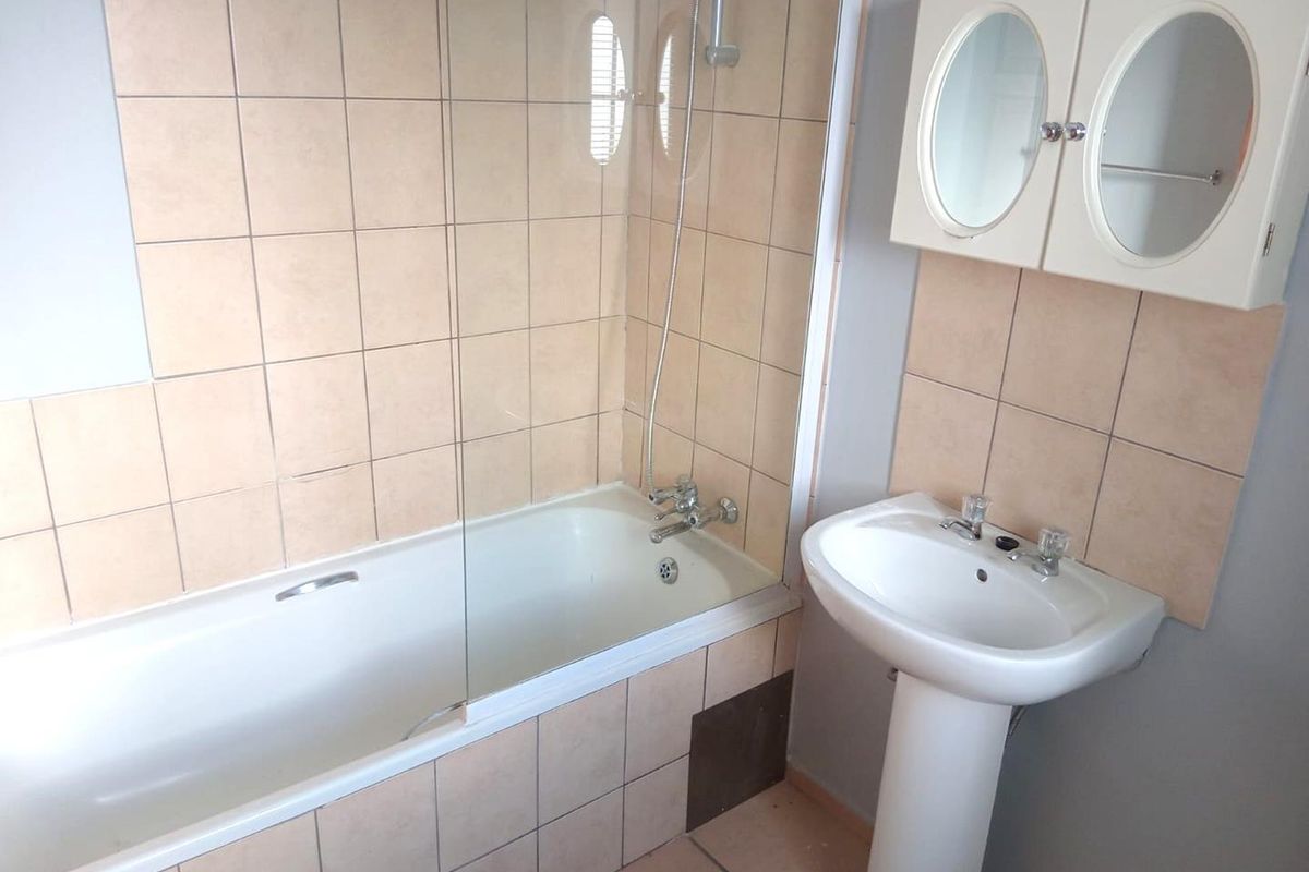 A functional bathroom featuring a bathtub with a glass shower screen, a pedestal basin, and a wall-mounted medicine cabinet.