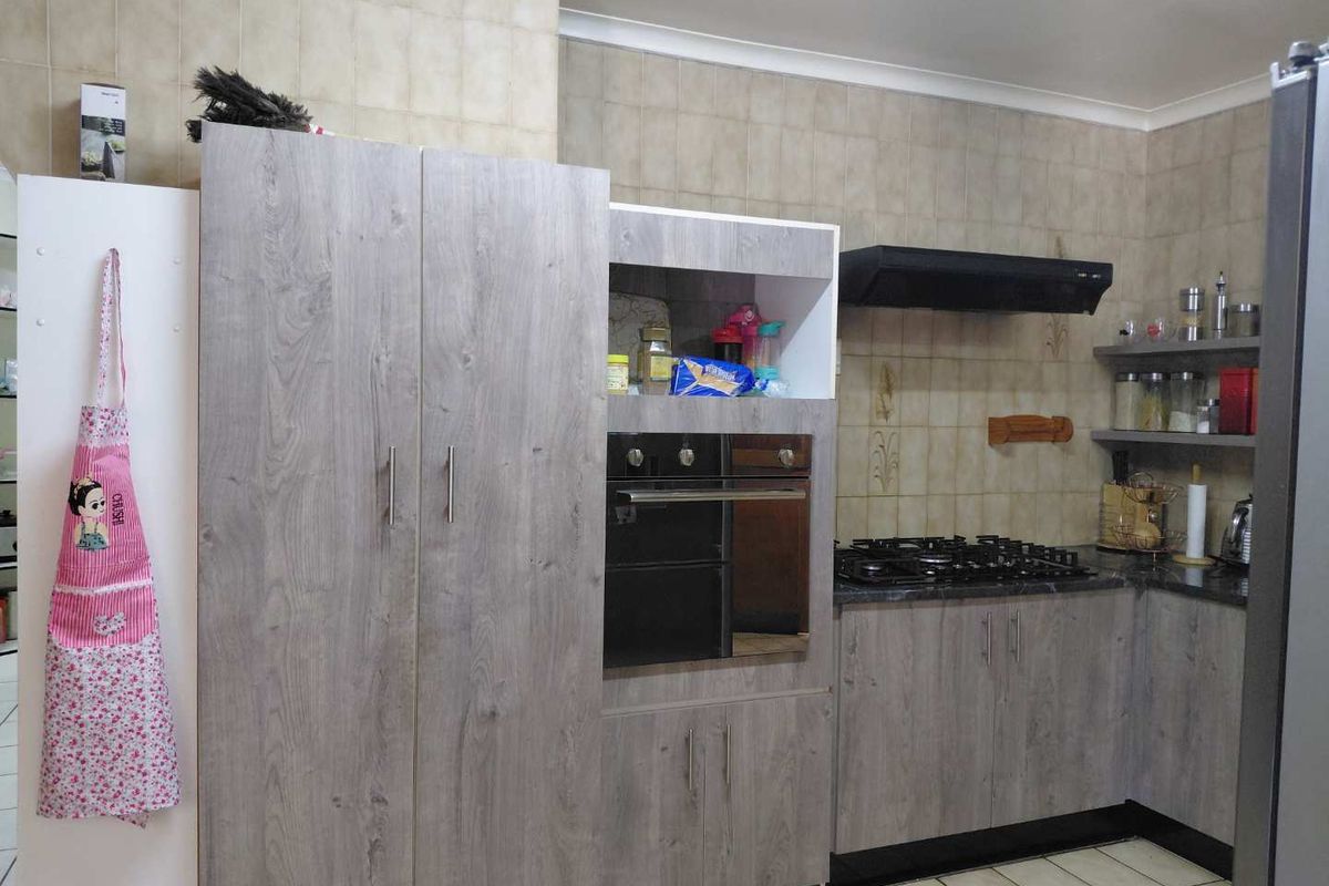 A functional kitchen featuring modern grey wood-grain cabinetry, a built-in oven, gas hob with extractor fan, and tiled backsplash.