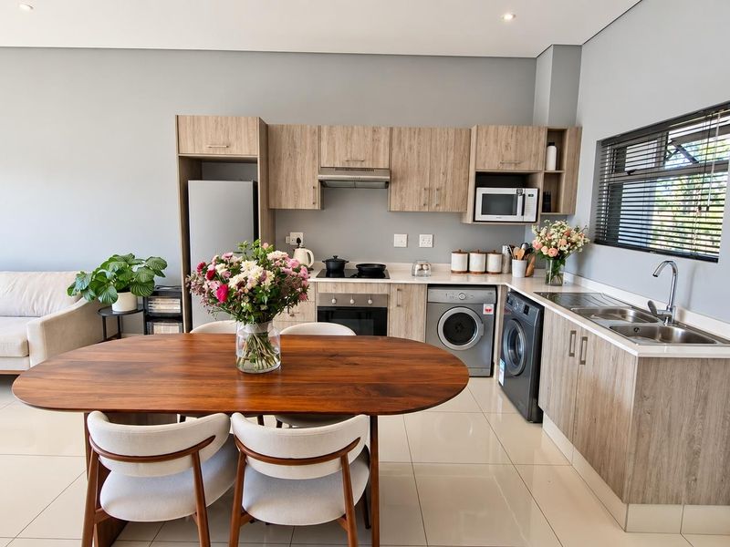 Modern open-plan living area featuring a well-appointed kitchen with wood-finish cabinetry, integrated appliances, and sleek tiled flooring throughout.