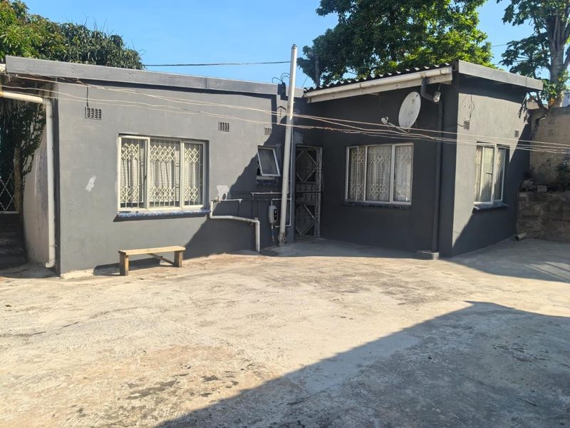 Rear exterior view of the house featuring dark grey painted walls, security bars on windows, and a concrete paved yard area.