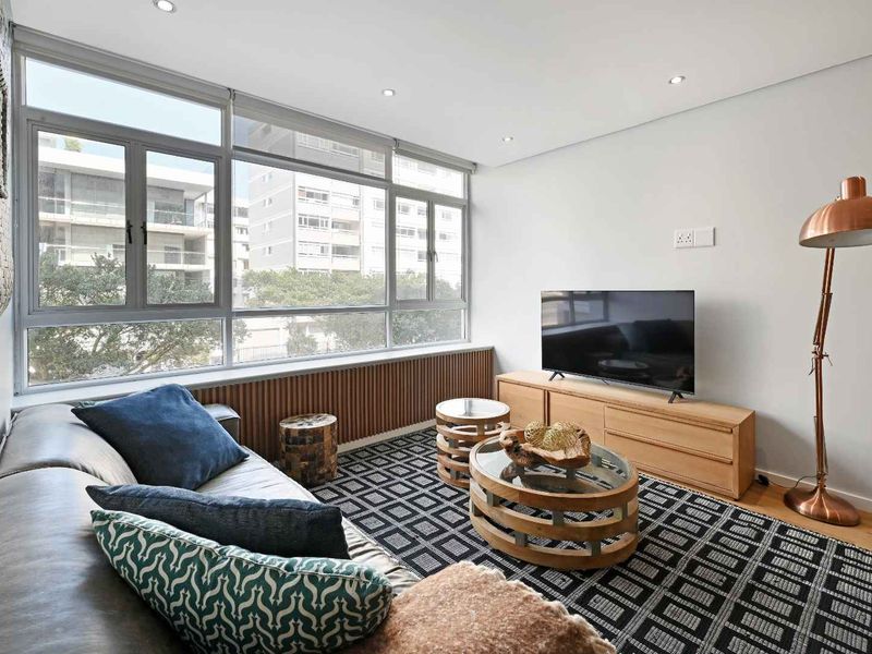 A bright and modern living room featuring large windows, timber-slat wall detailing, recessed lighting, and polished hardwood flooring.