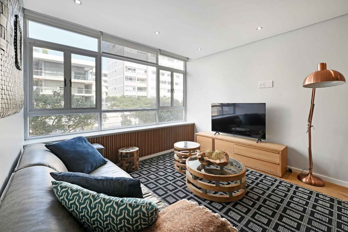 A bright and modern living room featuring large windows, timber-slat wall detailing, recessed lighting, and polished hardwood flooring.