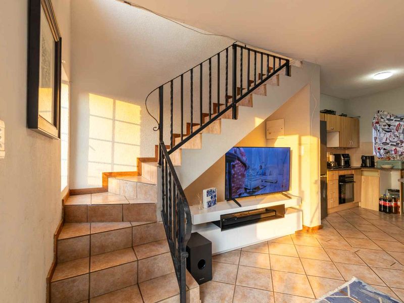 Open-plan living area featuring a tiled staircase with wrought iron railing, leading into a functional kitchen with built-in cabinetry and appliances.