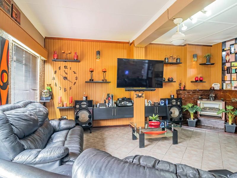 A living room featuring wood-paneled walls, a stone fireplace, and tiled flooring, offering a dated aesthetic with potential for modern updates.