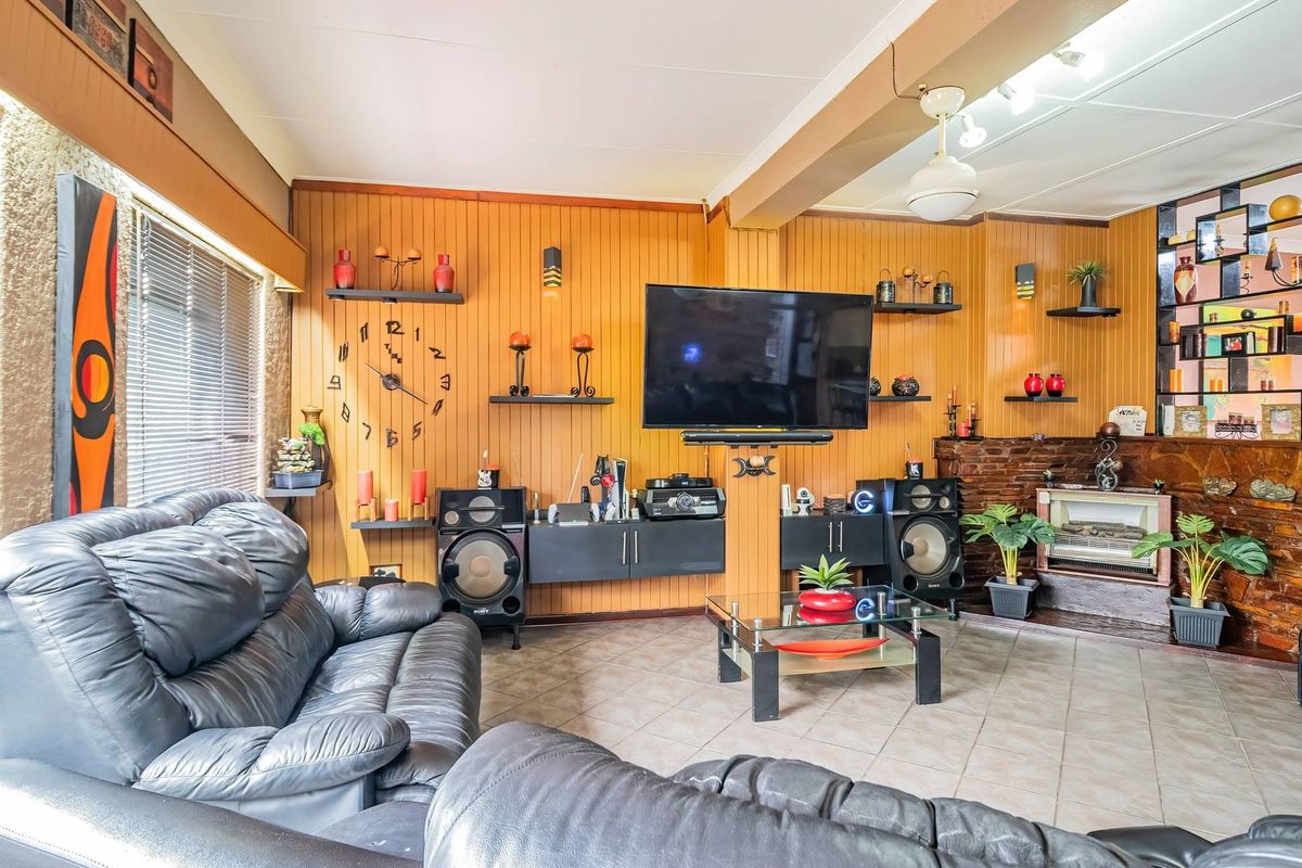 A living room featuring wood-paneled walls, a stone fireplace, and tiled flooring, offering a dated aesthetic with potential for modern updates.