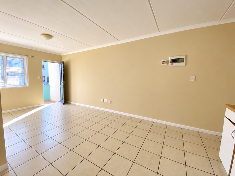 An empty open-plan living area featuring neutral wall paint, tiled flooring, and direct access to an outdoor balcony space.