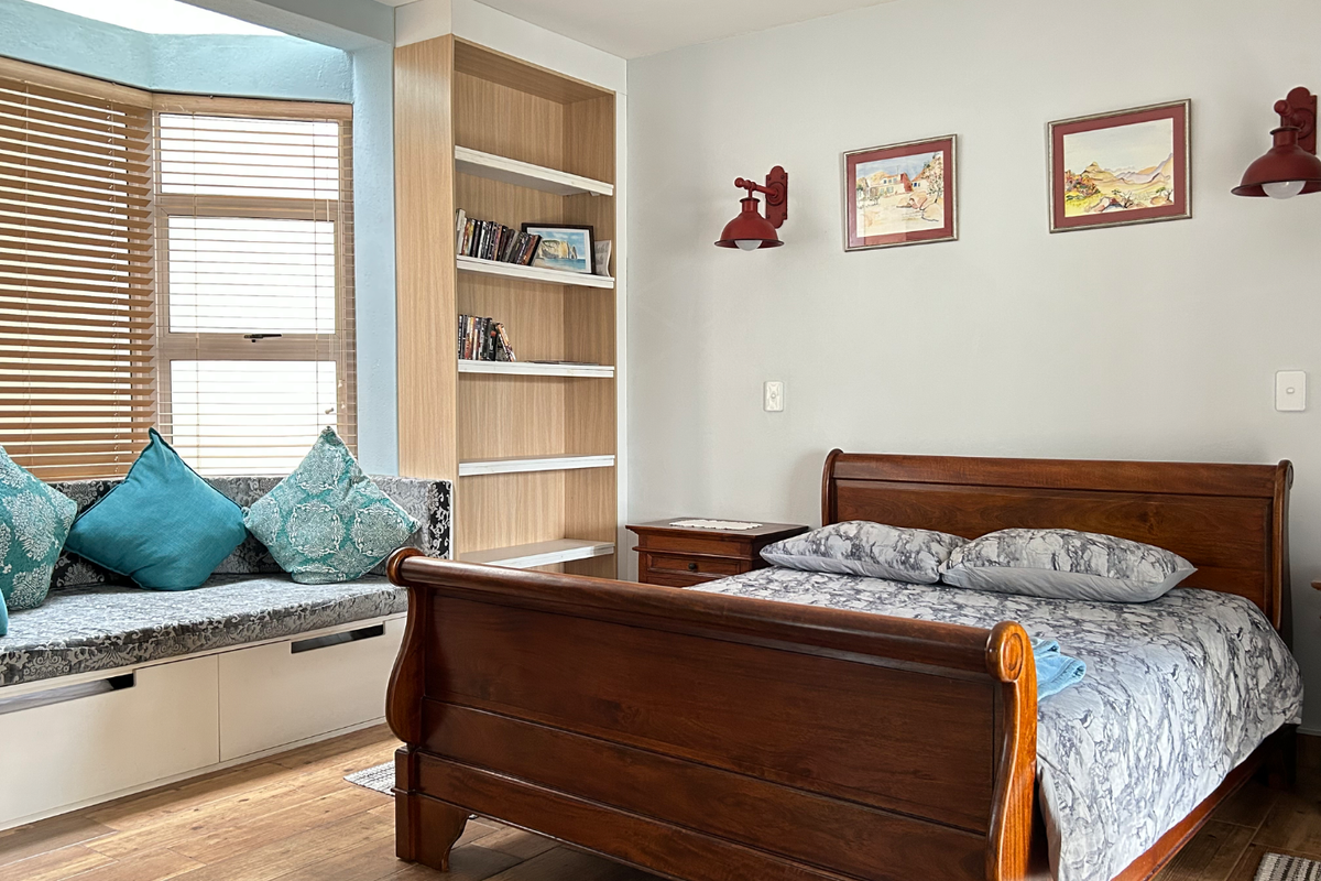 A well-maintained bedroom featuring a built-in window seat, integrated shelving unit, and warm wood-look flooring, creating a cozy and functional living space.