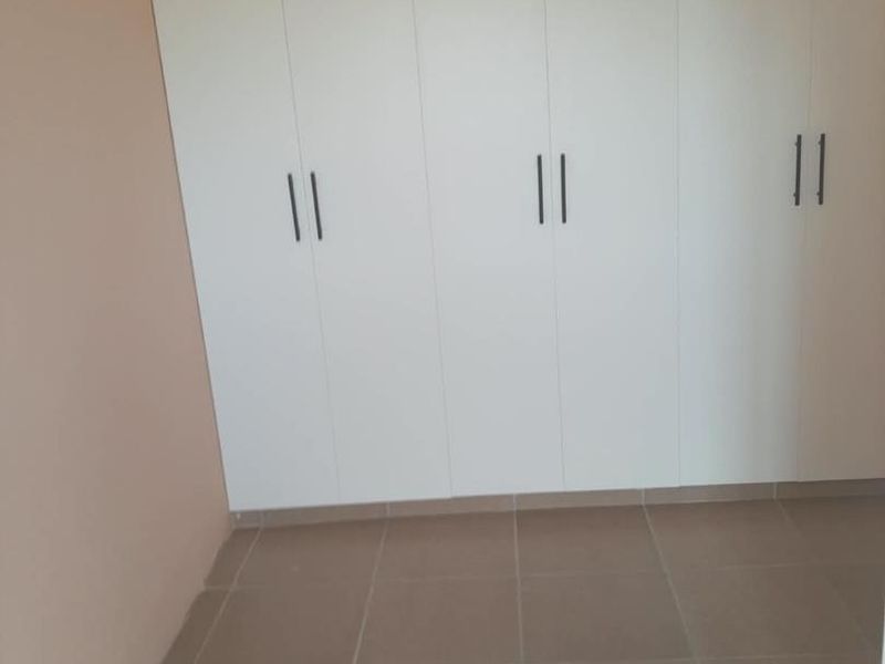 A clean, empty bedroom featuring neutral tiled flooring and modern white built-in cupboards with vertical handles.