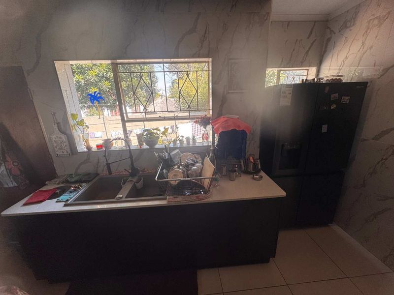 A functional kitchen area featuring a double basin sink with a modern mixer tap, marble-look wall tiling, and security bars on the window.