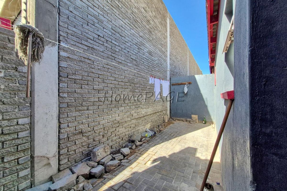 A narrow rear exterior courtyard featuring brick paving and high boundary walls, currently requiring clearing and maintenance to improve the outdoor space.