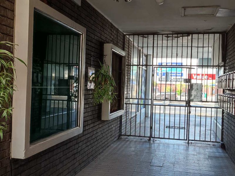 A secure apartment building entrance featuring dark brick walls, tiled flooring, and a metal security gate leading to the street.