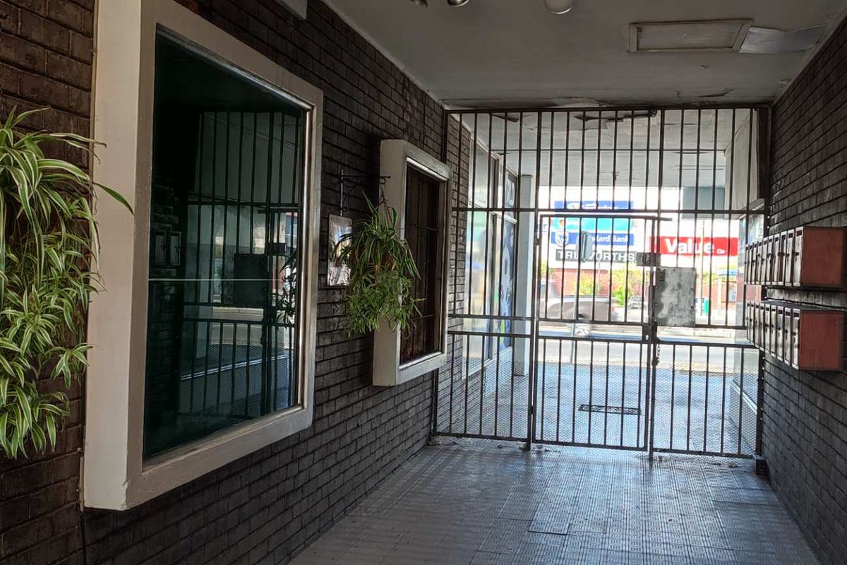A secure apartment building entrance featuring dark brick walls, tiled flooring, and a metal security gate leading to the street.