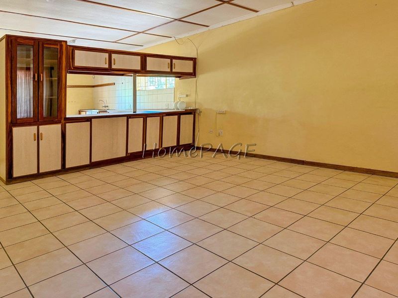 Spacious open-plan living and kitchen area featuring tiled flooring, built-in cabinetry, and a functional kitchen layout ready for modernization.