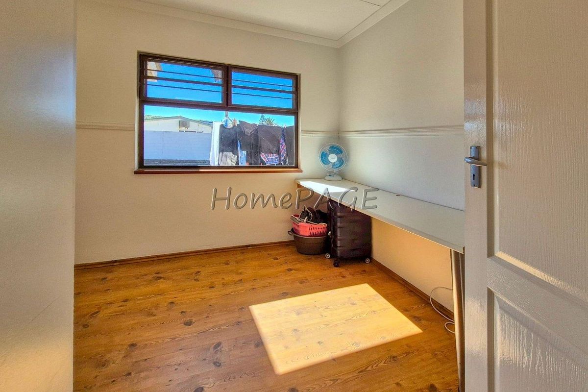 A functional bedroom or study space featuring timber flooring, a built-in desk, and a window overlooking the exterior area.