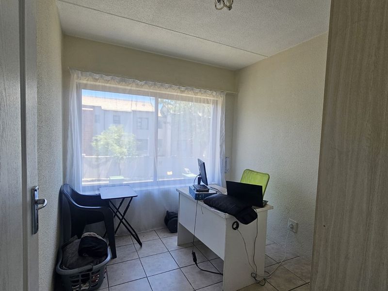 A compact bedroom featuring tiled flooring and a large window, providing natural light and a functional space for a home office or sleeping area.