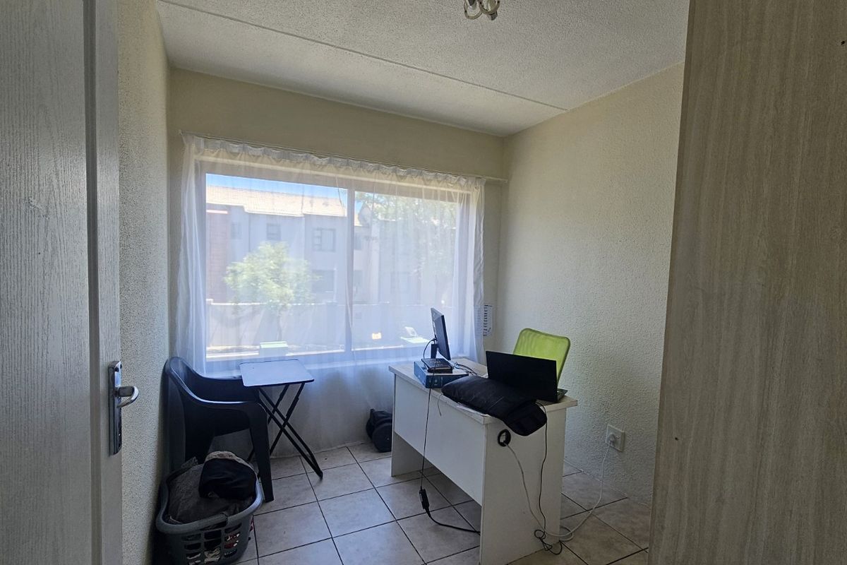 A compact bedroom featuring tiled flooring and a large window, providing natural light and a functional space for a home office or sleeping area.