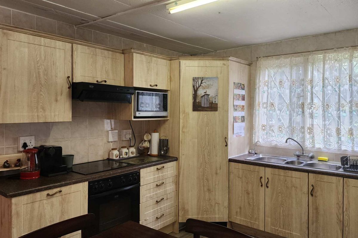 A functional kitchen featuring light wood-grain cabinetry, a built-in oven with hob, extractor fan, and a double-basin sink under a window.