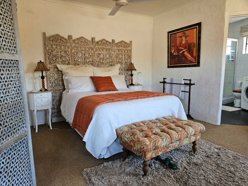 A bedroom featuring a ceiling fan and an en-suite bathroom access, with textured wall finishes and neutral carpeting.