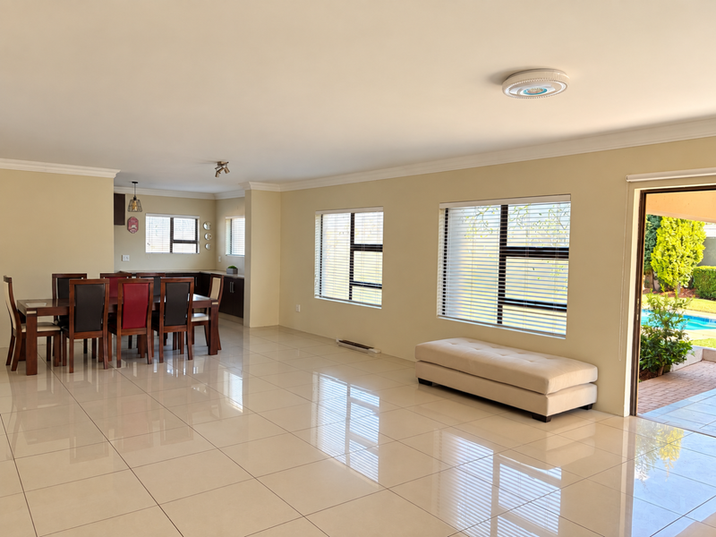 Spacious open-plan living and dining area featuring polished porcelain tiles, large windows with blinds, and direct access to the outdoor patio and pool area.