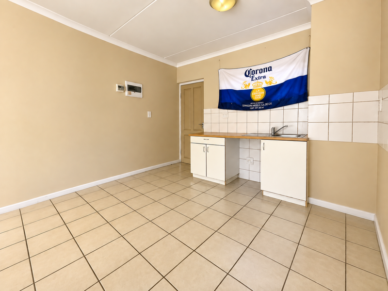 A compact, empty kitchen area featuring tiled flooring, basic cabinetry with a stainless steel sink, and a tiled backsplash.