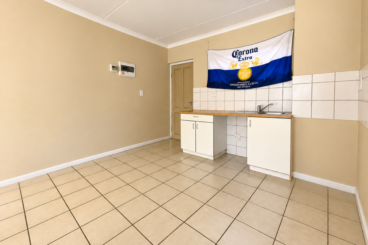 A compact, empty kitchen area featuring tiled flooring, basic cabinetry with a stainless steel sink, and a tiled backsplash.