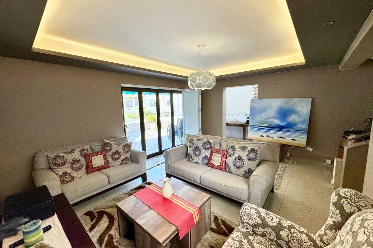 A comfortable living room featuring a recessed tray ceiling with integrated ambient lighting and large sliding glass doors leading to an outdoor patio area.