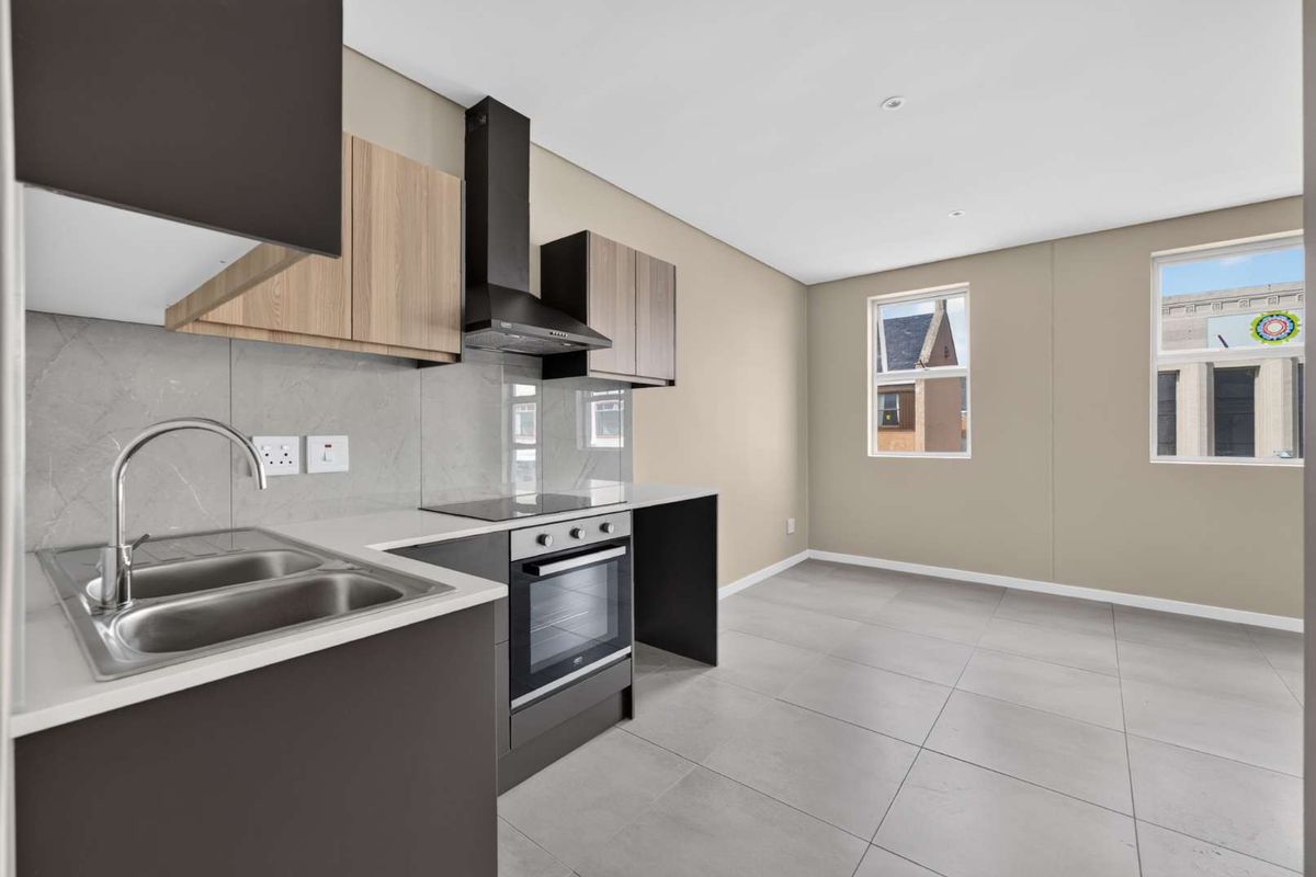 Modern open-plan kitchen featuring sleek cabinetry, stone countertops, integrated oven and hob, and neutral tiled flooring in a bright, well-maintained space.