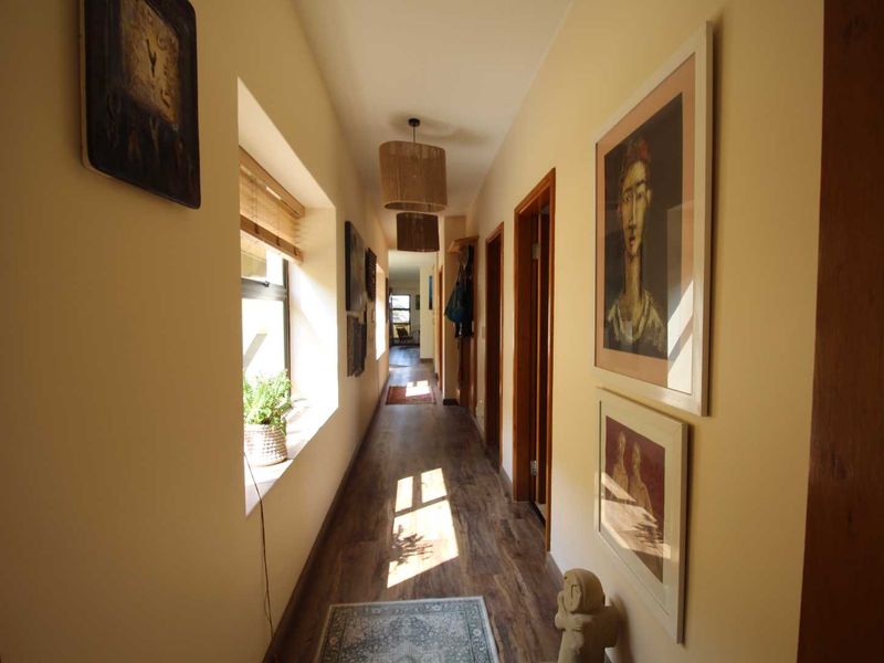 A well-lit hallway featuring laminate wood-look flooring, warm-toned walls, and multiple doorways leading to other areas of the apartment.