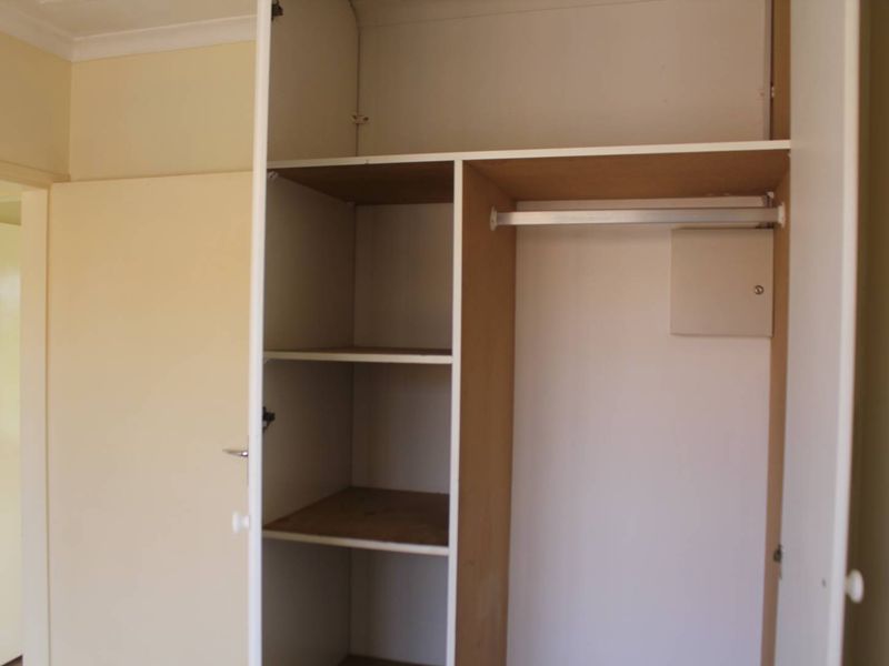 A bedroom featuring a built-in wardrobe with integrated shelving and a hanging rail, providing functional storage space.