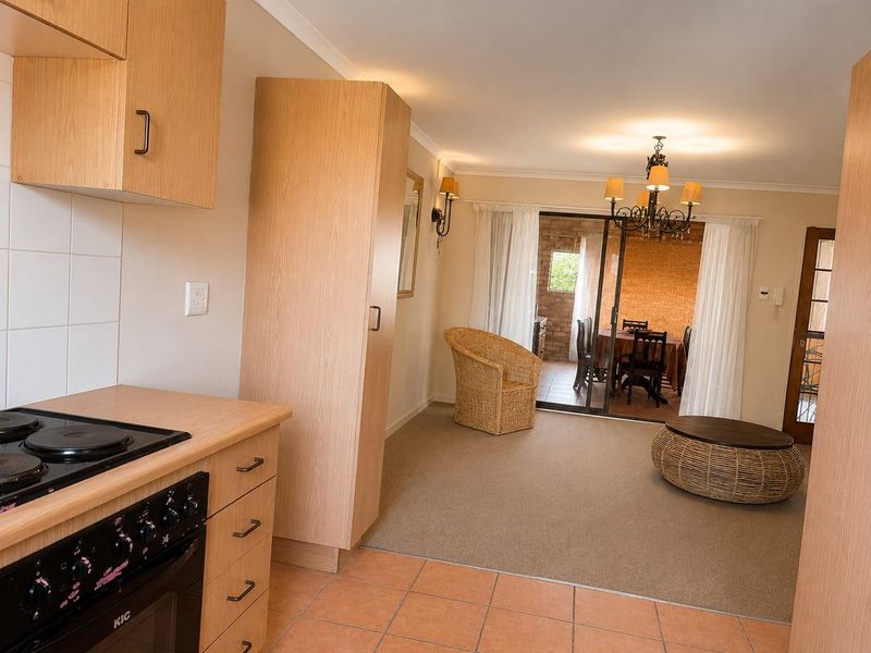 Open-plan living area featuring a functional kitchen with built-in cabinetry and stove, flowing into a carpeted lounge area with access to a covered patio.