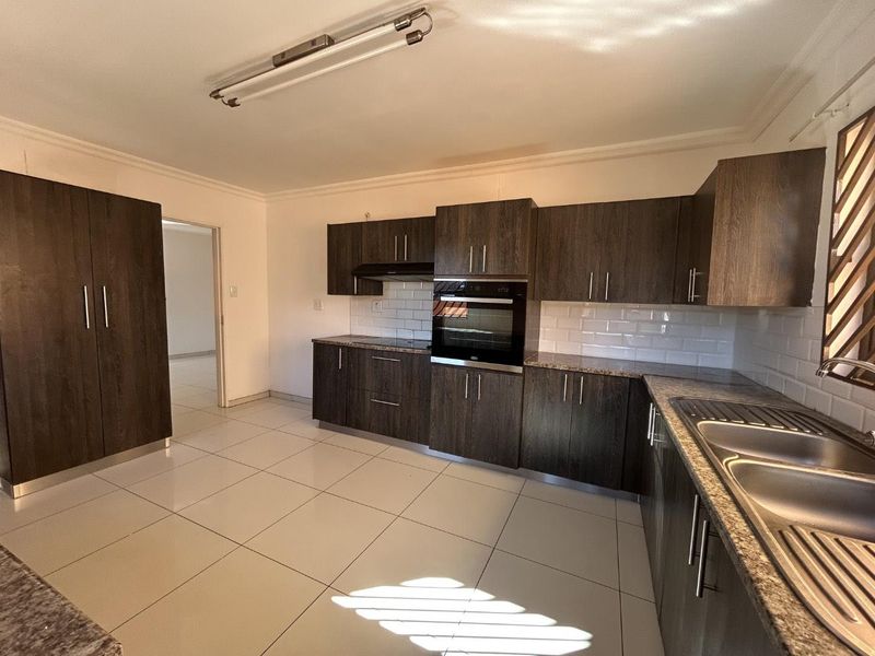 A clean, modern kitchen featuring dark wood cabinetry, granite countertops, subway tile backsplash, and built-in oven with extractor fan.
