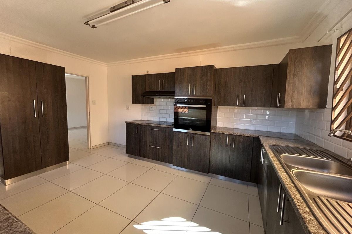A clean, modern kitchen featuring dark wood cabinetry, granite countertops, subway tile backsplash, and built-in oven with extractor fan.