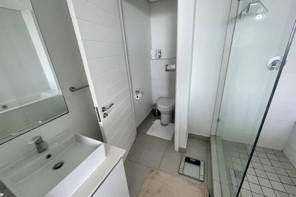A modern bathroom featuring a vanity with basin, a glass-enclosed shower, and a separate toilet area with neutral tiling.