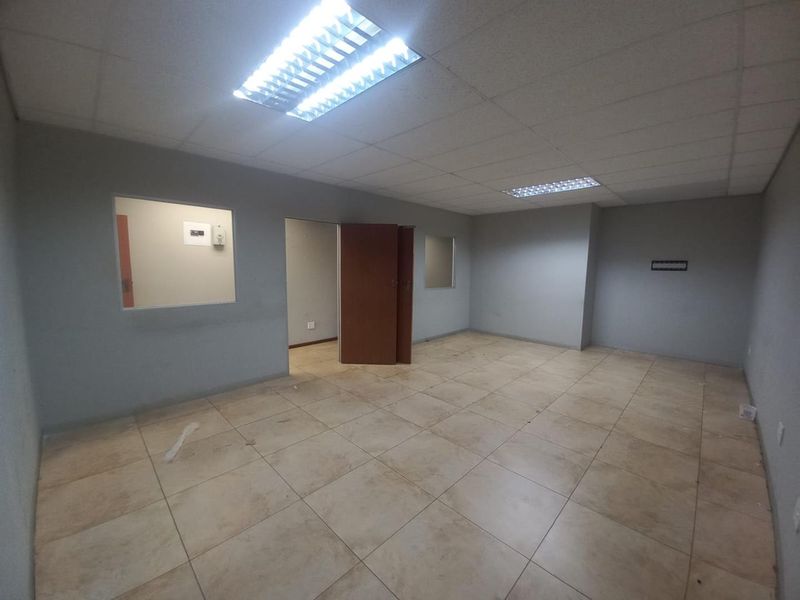 An empty, open-plan office space featuring neutral wall finishes, ceramic tiled flooring, and suspended ceiling lighting, suitable for various business configurations.
