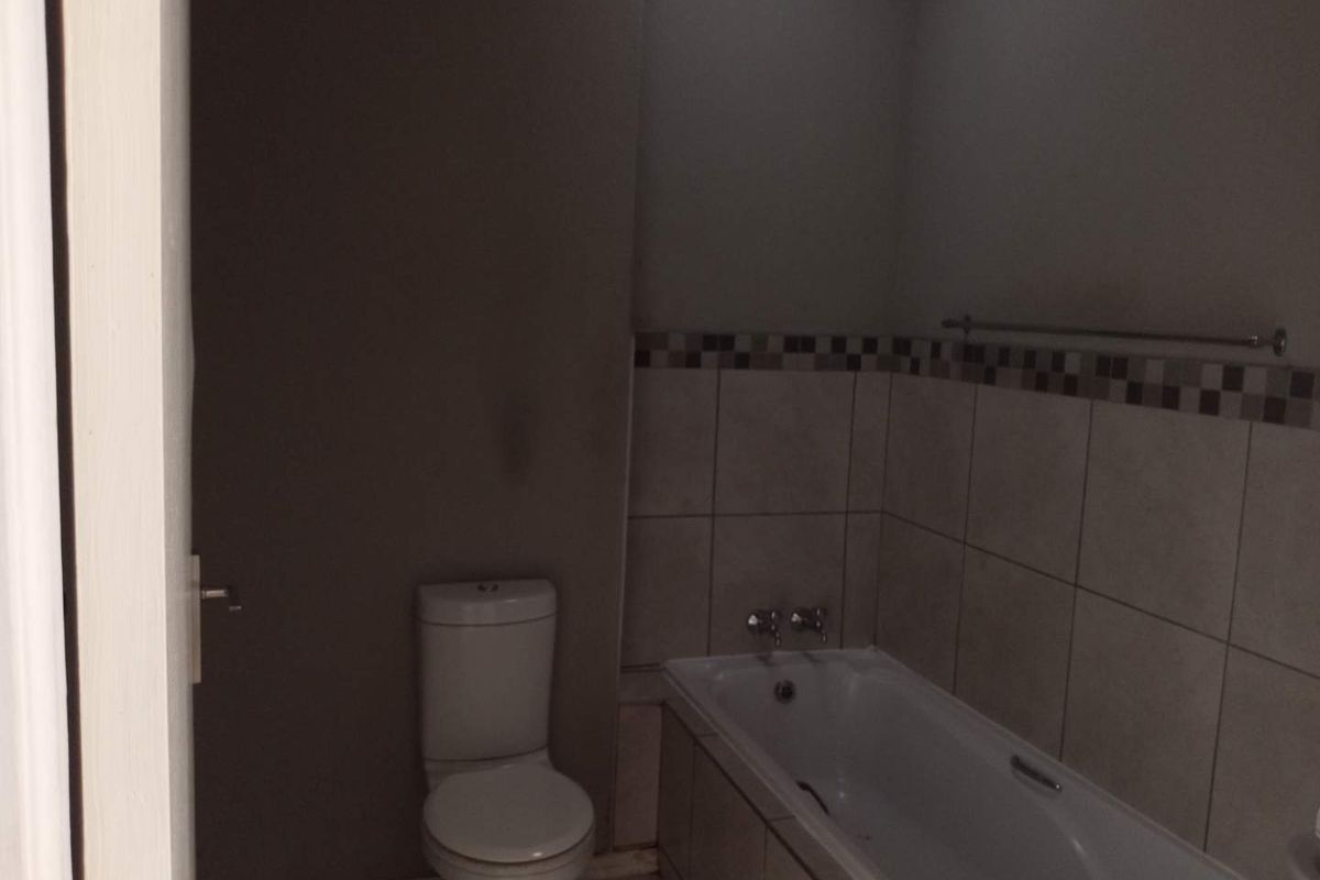 A functional bathroom featuring a standard bathtub with wall-mounted taps and a toilet, finished with neutral wall tiles and a decorative border.