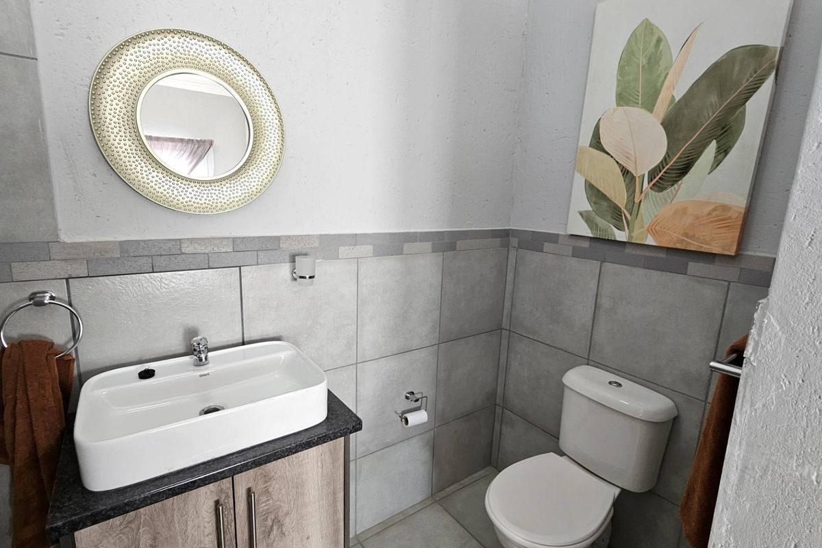 A clean and functional bathroom featuring a modern vanity with a vessel sink, a wall-mounted mirror, and a standard toilet with grey tiled walls.